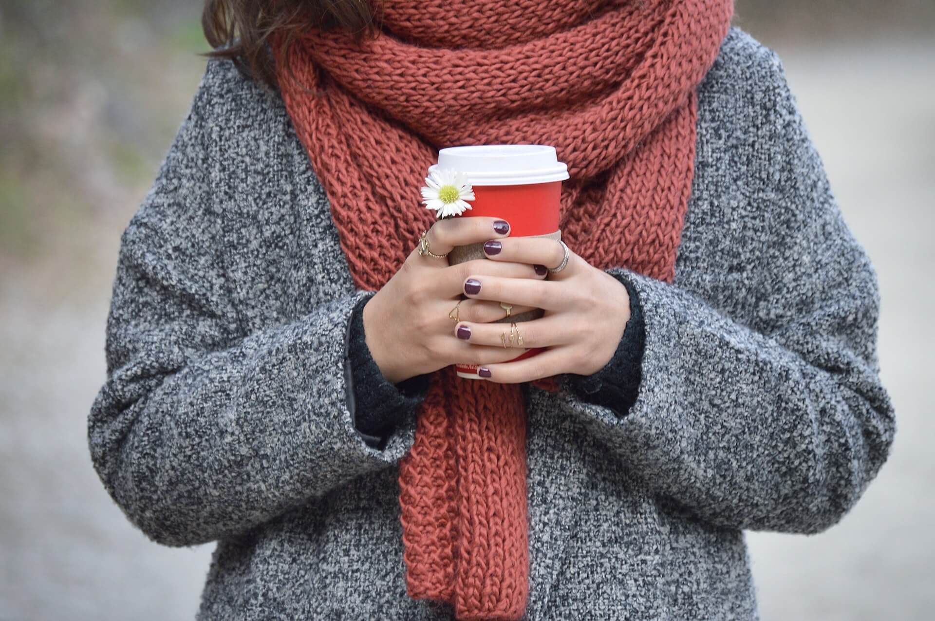 a lady holding a coffee mug, she is rugged up wearing a scarf and warm jacket