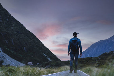 A silhouette of a man on a hike. He's looking out toward a purple/blue sky and mountains.